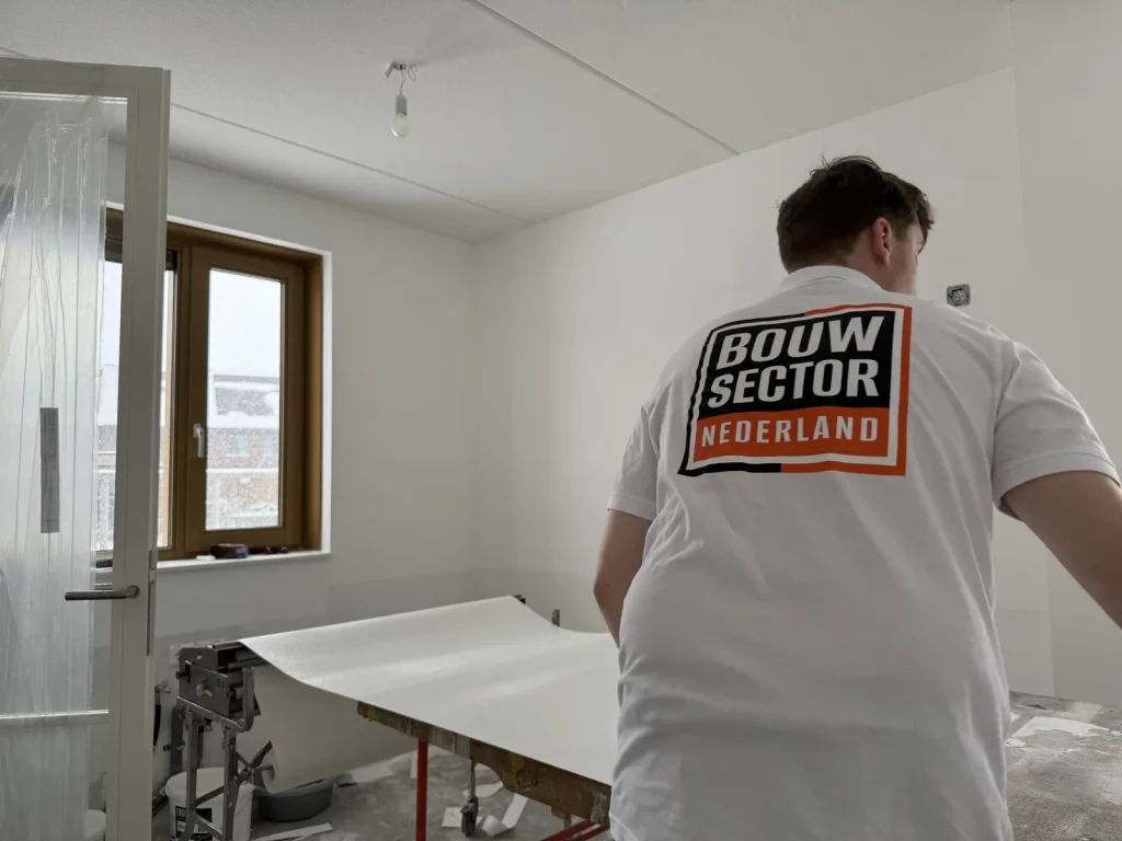 Behanger van Bouwsector Nederland in wit poloshirt legt een baan wit weefsel op de plaktafel in een kale nieuwbouwkamer