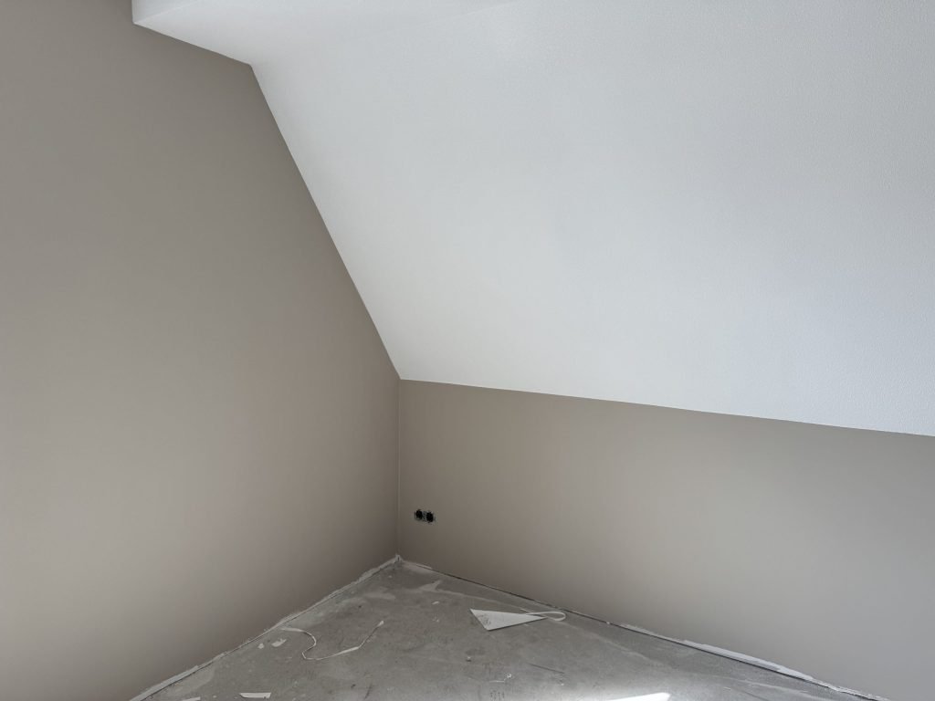 Kamer onder een schuin dak met egaal beige afgewerkte wanden en een wit plafond in een nieuwe woning
