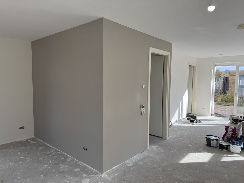 Open nieuwbouwbenedenverdieping met een strak grijs afgewerkte wand rond de trapkast en verfemmers op de betonvloer