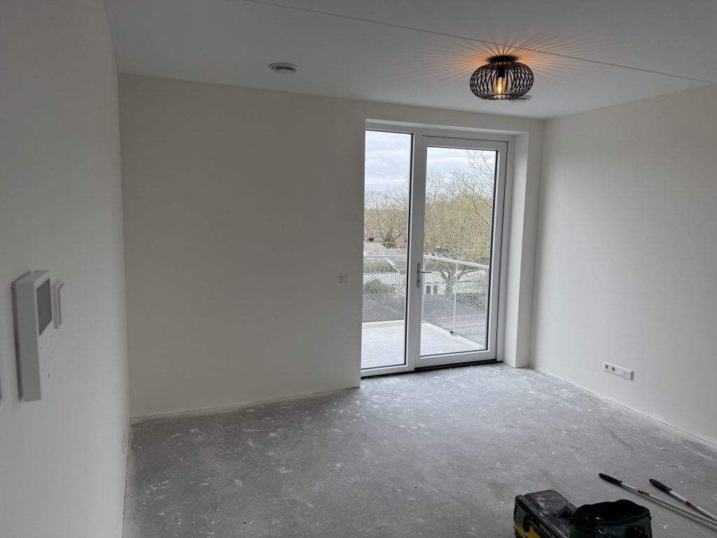 Lege kamer in een nieuw appartement met gladde witte wanden en openslaande deuren naar een balkon